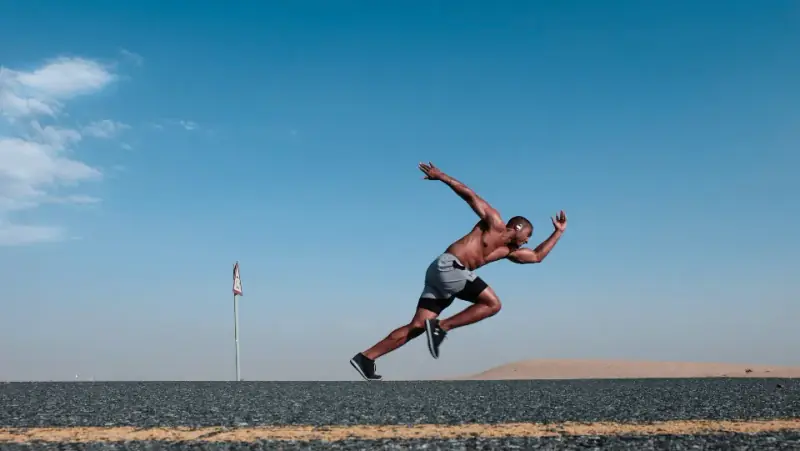 A sprinter launching forward on an empty track under a blue sky