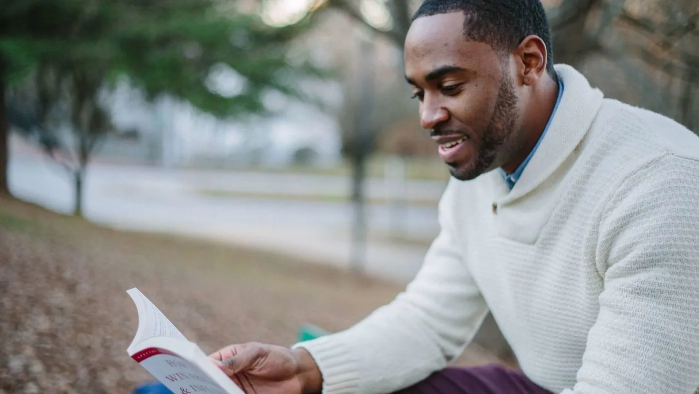 A man reading a book outdoors on a bright day