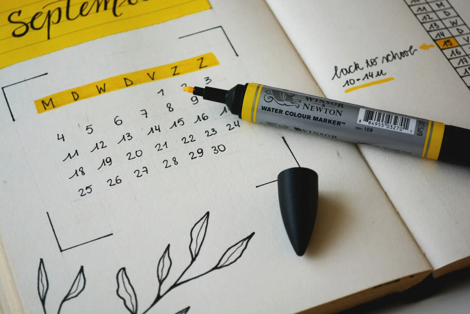 A hand drawn monthly calendar in a notebook with a marker beside it