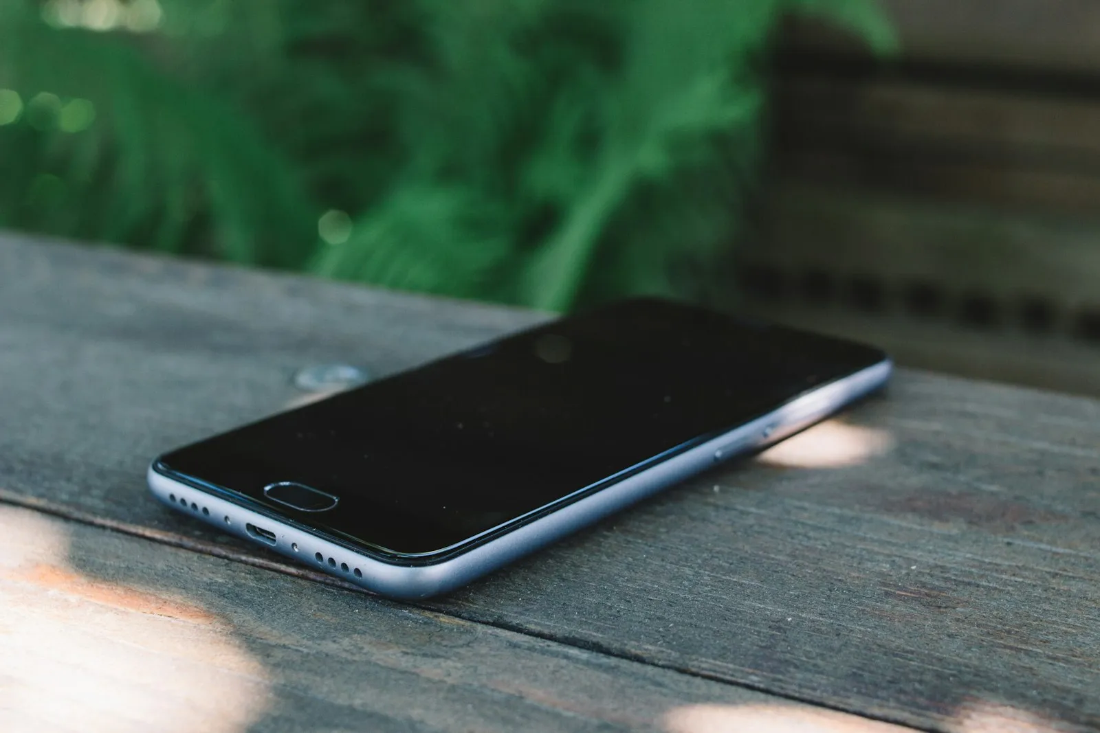 A phone lying face down on a dark wooden table, out of reach