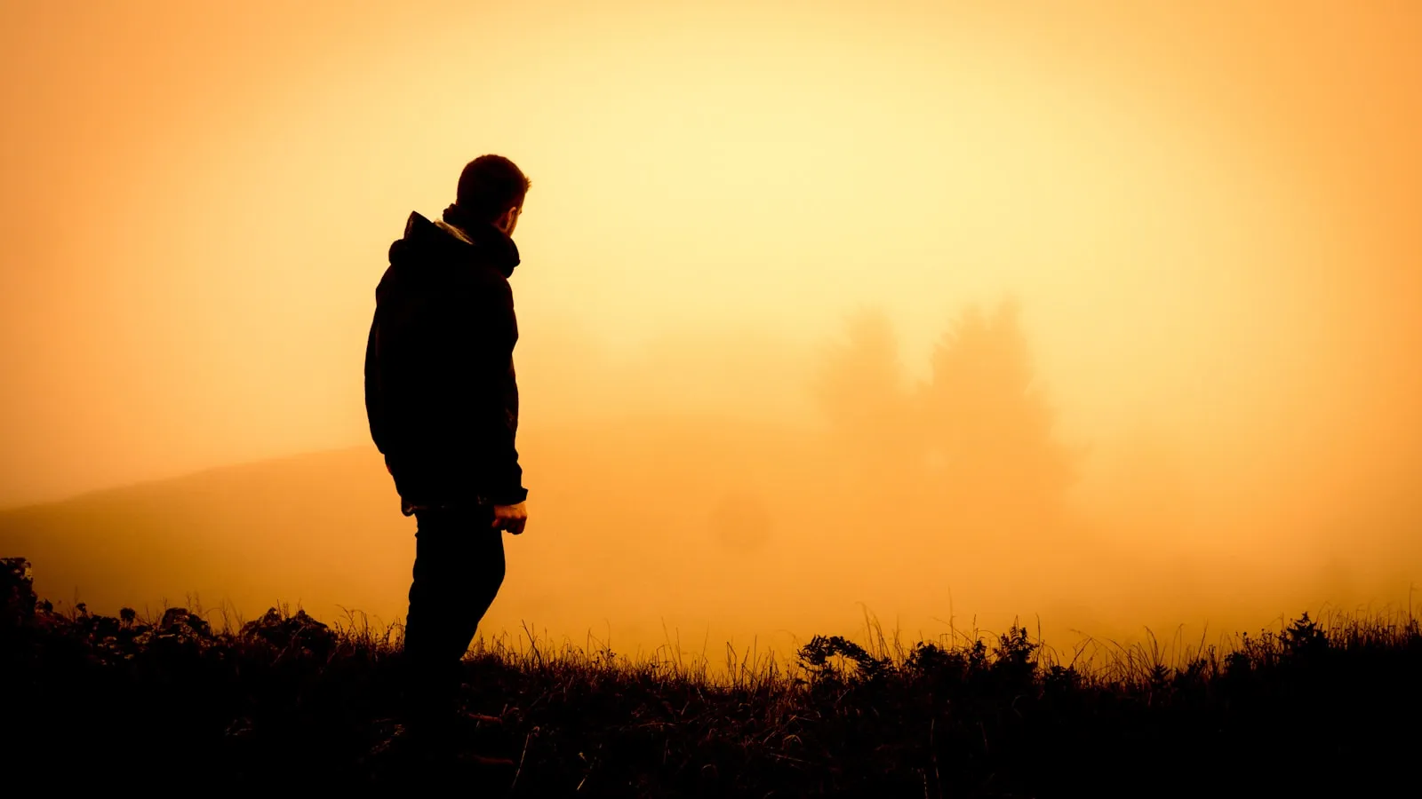 A person standing on a ridge at sunrise, backlit by low golden light