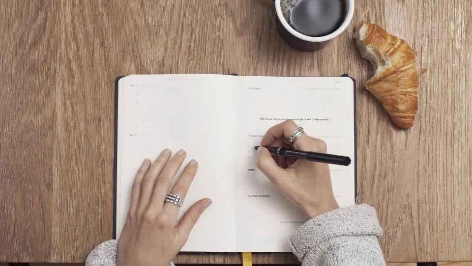 A notebook open on a desk beside a cup of coffee