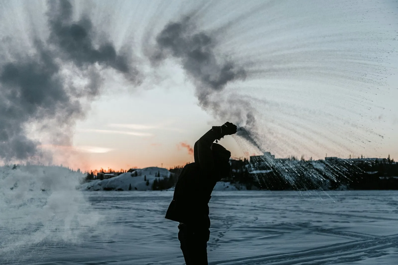 A figure throwing water into freezing air at sunset