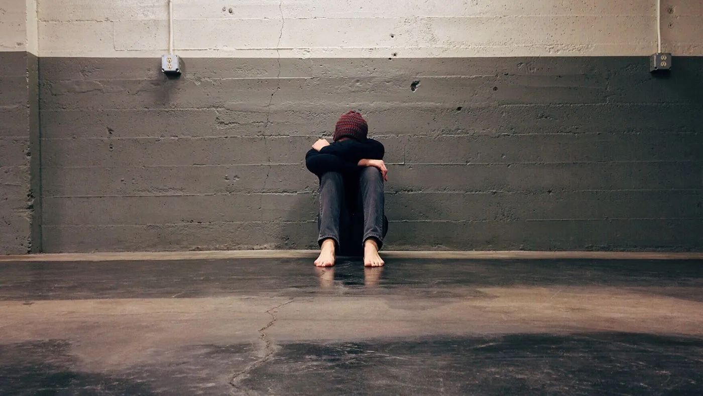 A figure sitting alone against a bare wall
