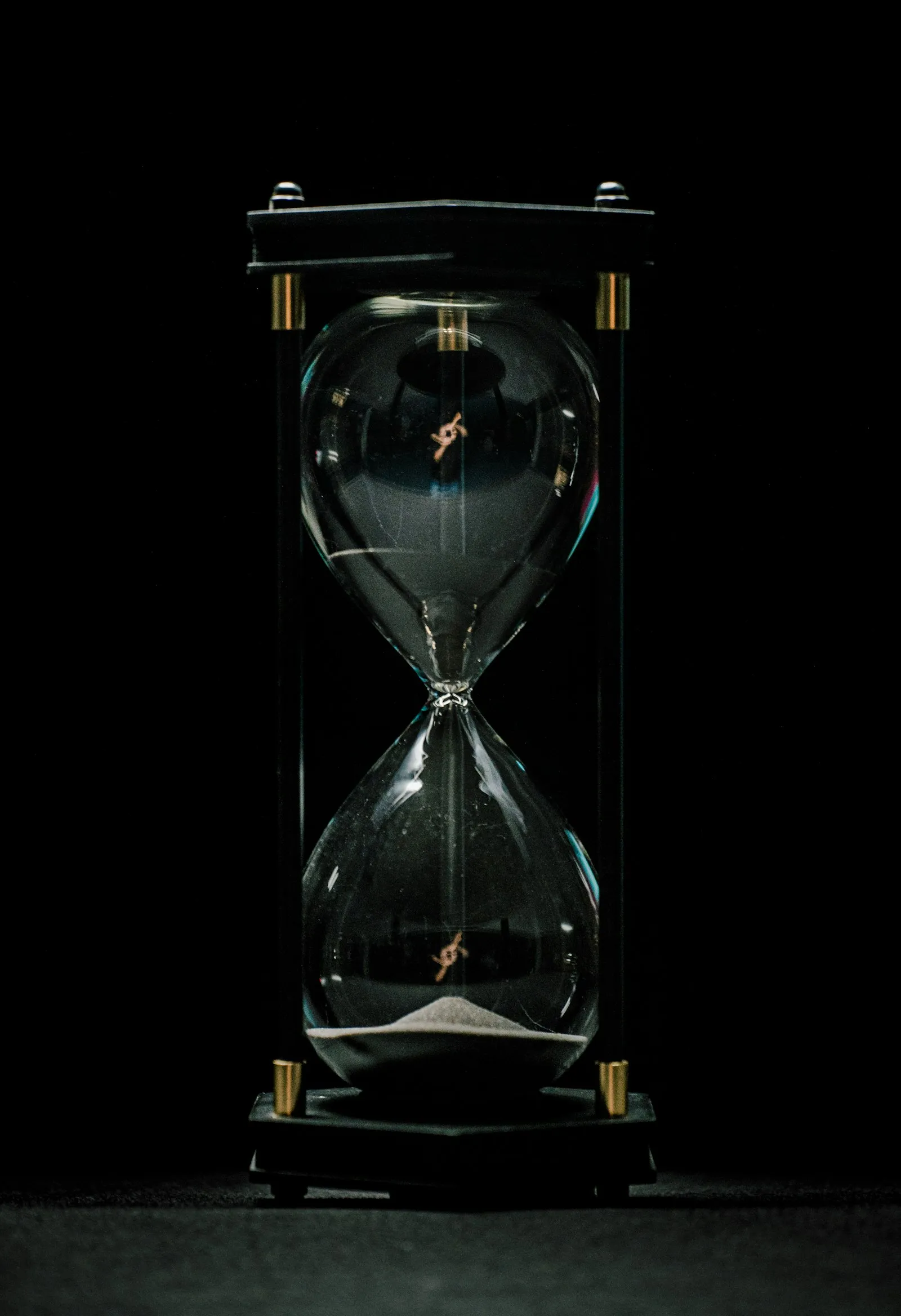 An hourglass with the sand running through it, lit against a dark background