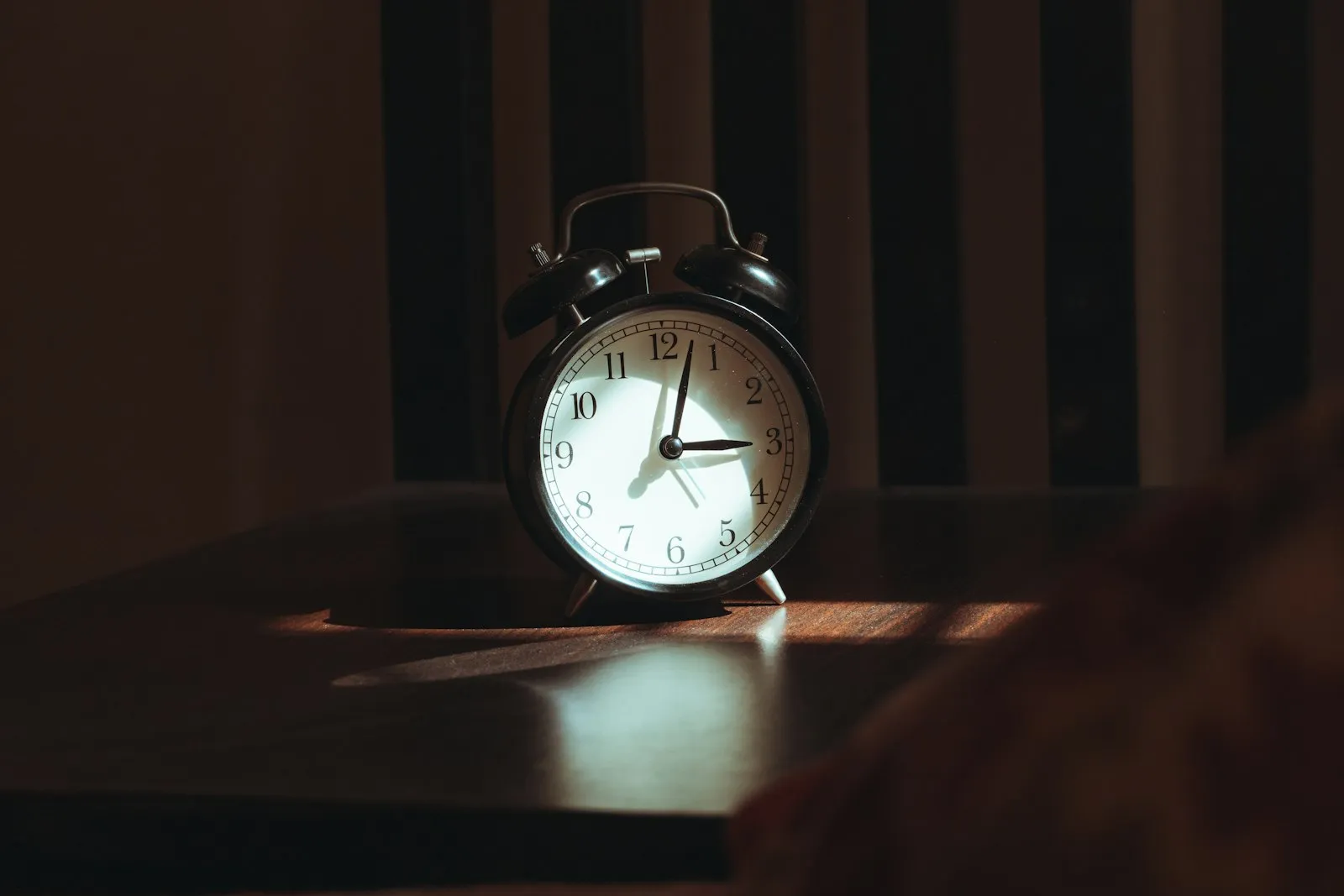 An alarm clock on a bedside table catching the first light of the morning